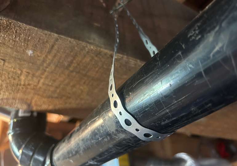 Use metal plumbing strapping for installing ABS drains with a 1/4 inch slope - Image © Mike Reynolds